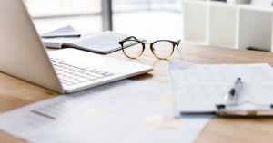 机の上にパソコン、ノート、メガネ、紙